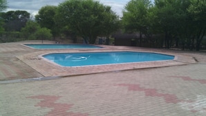 Deux piscines rectangulaires bordées de briques, entourées d’arbres et d’une zone dallée.