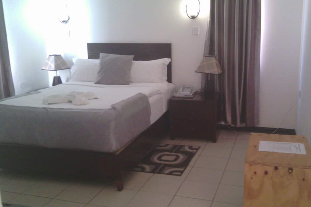 Habitación de hotel con cama, dos lámparas de noche, mesita de noche con teléfono, una pequeña caja de madera y una alfombra estampada.