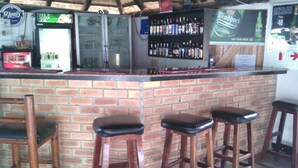 Un espace bar avec un comptoir en briques, des tabourets et des étagères remplies de bouteilles d’alcool.