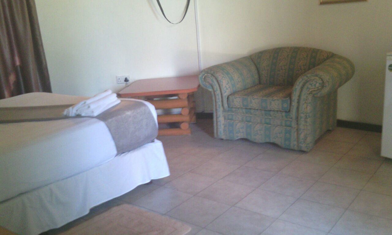 Una habitación con cama, una silla, una mesita y un enchufe.