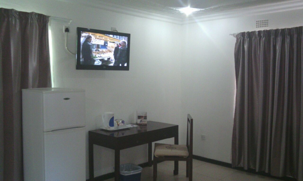 Une petite pièce avec un téléviseur fixé au mur, une table avec une chaise, un réfrigérateur et un rideau.