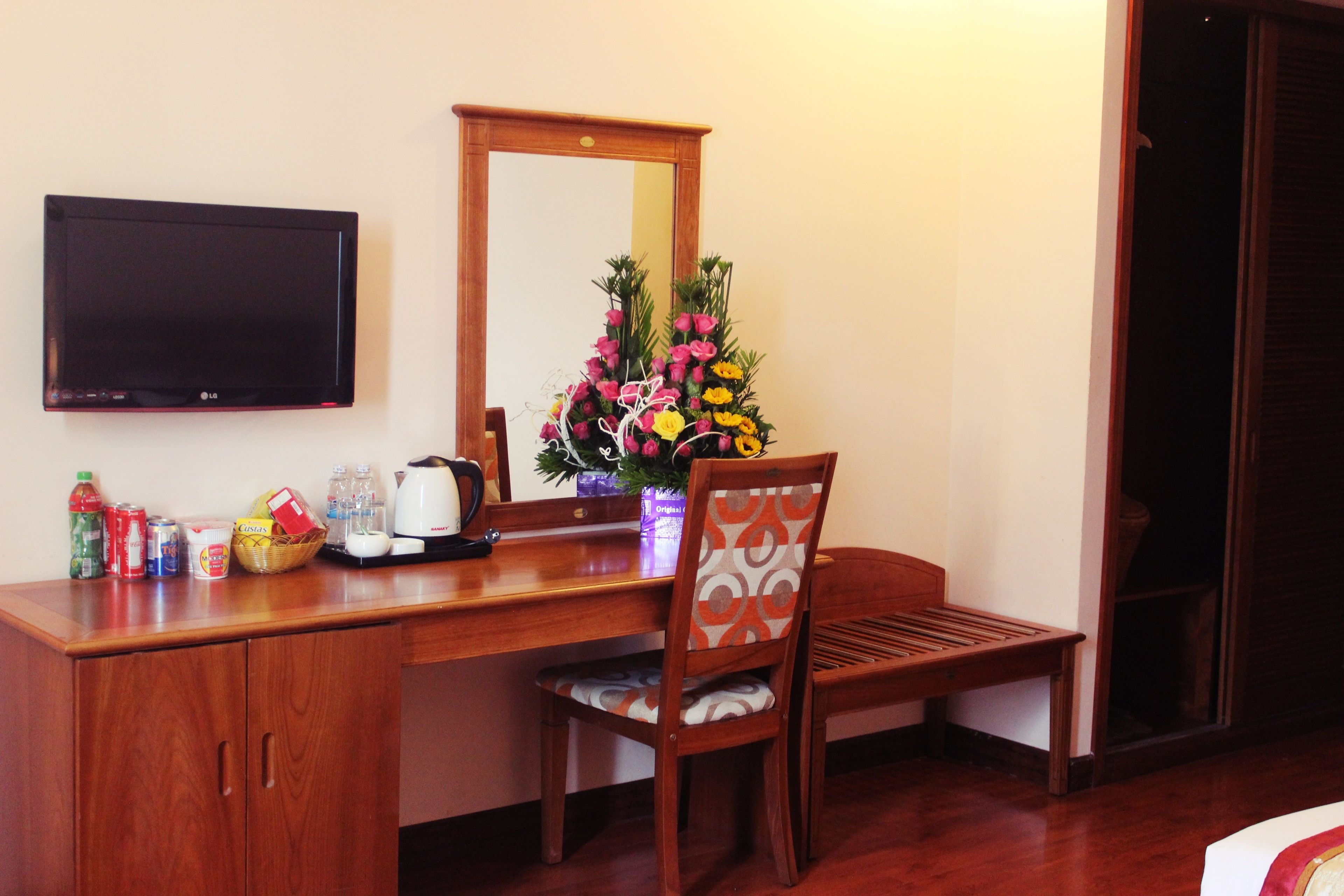 Une chambre d’hôtel avec un bureau en bois, une chaise, un téléviseur à écran plat, un miroir et un arrangement floral.