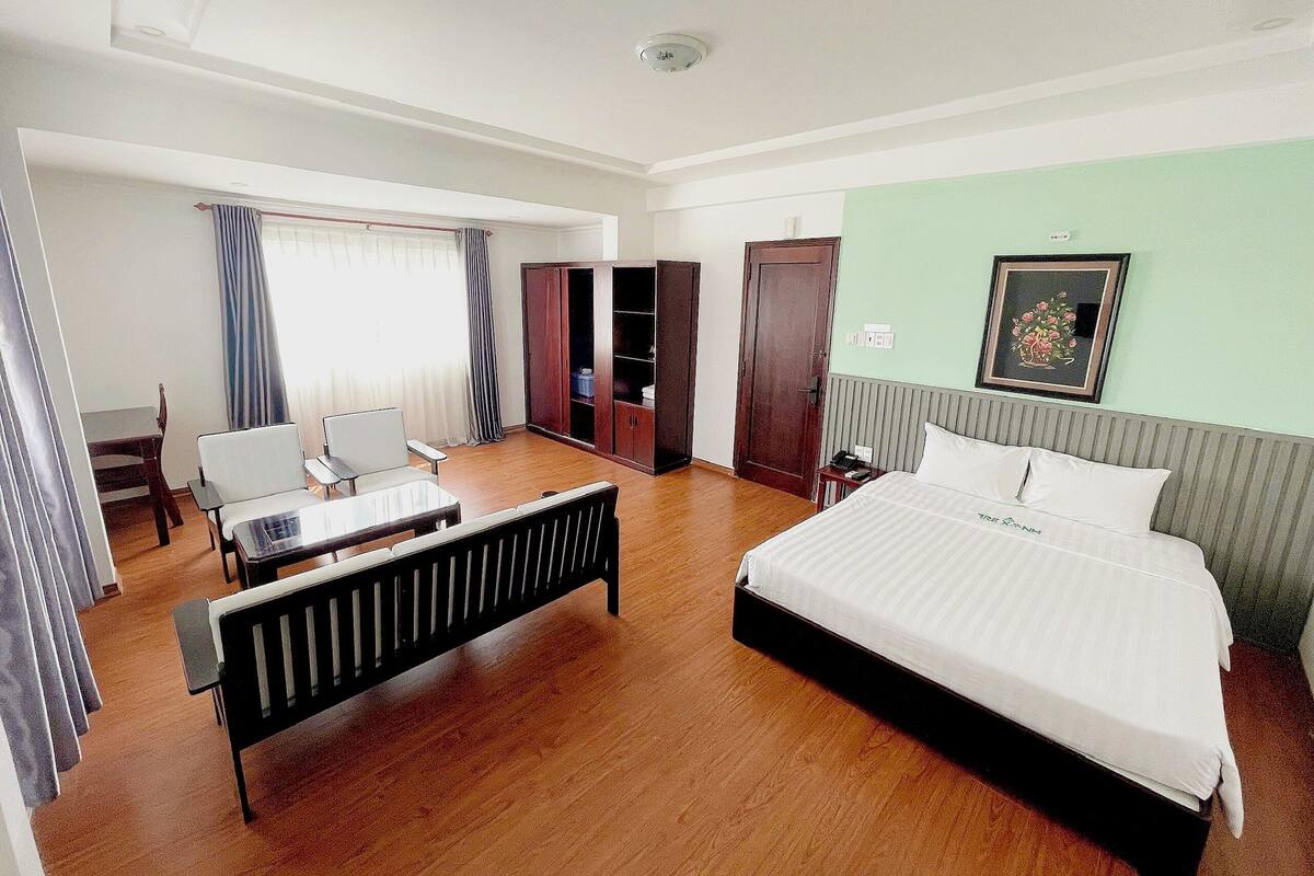 Quarto de hotel com cama, escrivaninha, cadeira, guarda-roupa e janela com cortinas.