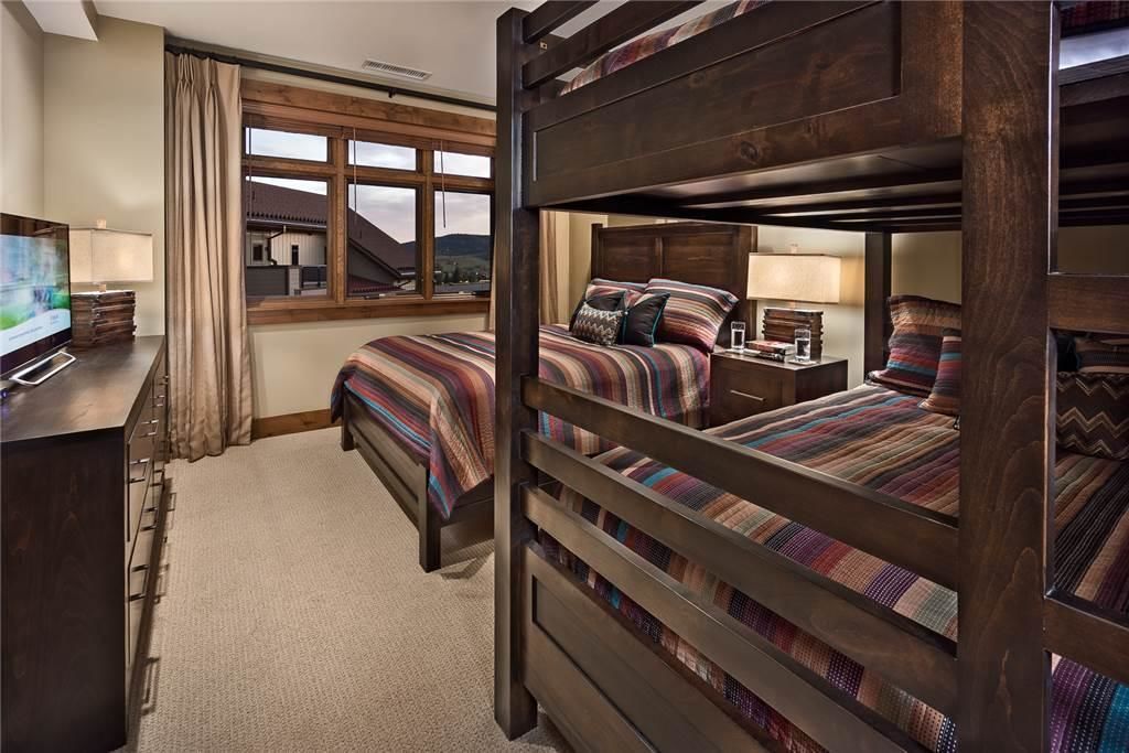 A bedroom with bunk beds, a desk with a TV, and a window with a view of a building and mountains.