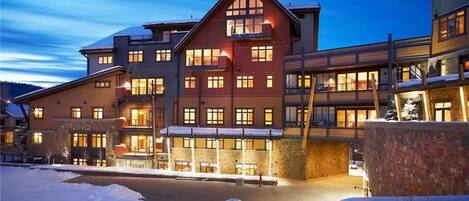 Un hotel de varios pisos con un edificio central destacado, múltiples balcones y un terreno cubierto de nieve.