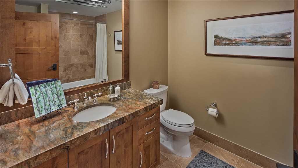 A bathroom with a marble sink, wooden cabinets, a toilet, and a framed picture on the wall.