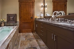 A bathroom with a wooden door, a bathtub, a sink with a mirror, and a vanity with drawers. - Elk Mountain 610 4 BedroomCondo By Moving Mountains (Steamboat Springs)