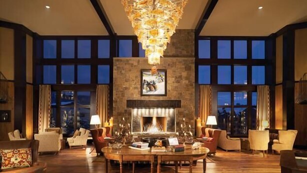 A spacious living room with a fireplace, large windows, and a chandelier. - Mount Yale 611 4 BedroomCondo By Moving Mountains (Steamboat Springs)