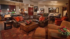 A spacious living room with a leather sofa, a coffee table with decorative items, and a dining area with a chandelier. - Diamond Peak Penthouse 616 4 BedroomCondo By Moving Mountains (Steamboat Springs)