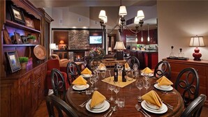 A dining area with a round table set for six, surrounded by chairs. A fireplace is visible in the background, and there are various decorative items on shelves. - Diamond Peak Penthouse 616 4 BedroomCondo By Moving Mountains (Steamboat Springs)