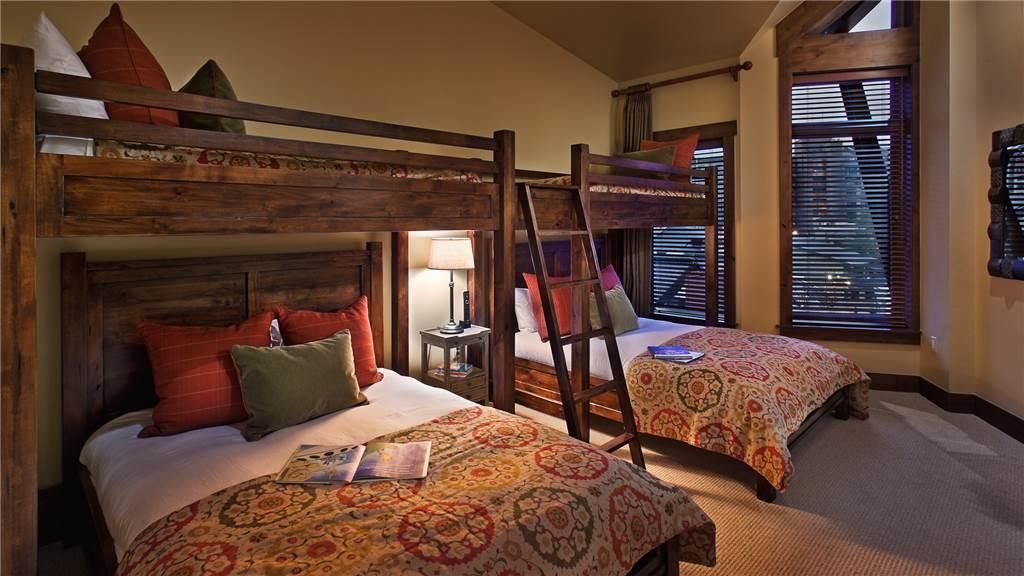 Une chambre avec deux lits superposés, une table de chevet avec une lampe et une fenêtre avec des stores.