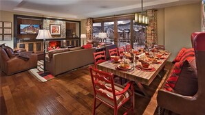 A dining area with a wooden table set for a meal, red chairs, and a view of the mountains through large windows. - Emerald Mountain 702 4 BedroomCondo By Moving Mountains (Steamboat Springs)