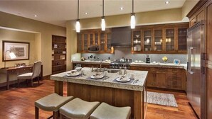 A modern kitchen with wooden cabinets, a central island with bar stools, a microwave, and a stainless steel refrigerator. - Quandary Peak Penthouse 704 4 BedroomCondo By Moving Mountains (Steamboat Springs)