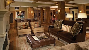 A spacious living room with a brown leather sofa, striped armchairs, and a brown ottoman. There are bookshelves in the background and a large painting on the wall. - Lone Star Mountain 709 4 BedroomCondo By Moving Mountains (Steamboat Springs)