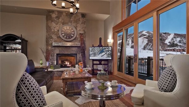Una sala de estar acogedora con chimenea, asientos cómodos, una mesa de centro y un ventanal con vistas a un paisaje montañoso nevado.