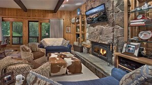 A cozy living room with a stone fireplace, wooden walls, and a large TV mounted above it.