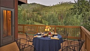 A dining area with a table set for two, overlooking a forested hillside.