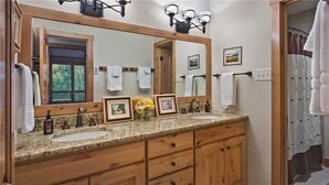 A bathroom with two sinks, wooden cabinets, a large mirror, and framed pictures on the countertop.