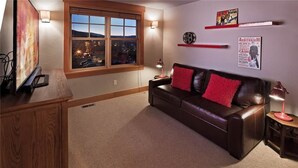 A cozy living room with a leather couch, a TV, and a window overlooking a cityscape. - Sunshine Peak Chalet 4 BedroomHoliday home By Moving Mountains (Steamboat Springs)