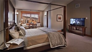 A bedroom with a large bed, a TV, a desk with a lamp, and a view of a cityscape through a window. - Sunshine Peak Chalet 4 BedroomHoliday home By Moving Mountains (Steamboat Springs)