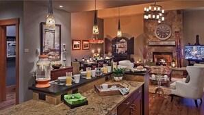 A modern kitchen with a central island, pendant lighting, and a stone fireplace. - Sunshine Peak Chalet 4 BedroomHoliday home By Moving Mountains (Steamboat Springs)