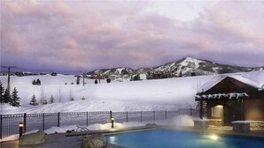 Un paisaje nevado con una piscina, una cabaña de madera y montañas al fondo.