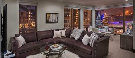 A modern living room with a sectional sofa, a glass coffee table, and a view of a decorated Christmas tree outside.