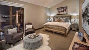 A bedroom with a large bed, two armchairs, a tufted ottoman, a nightstand, and a wall-mounted picture. - Wildhorse Chalet 3 BedroomHoliday home By Moving Mountains (Steamboat Springs)