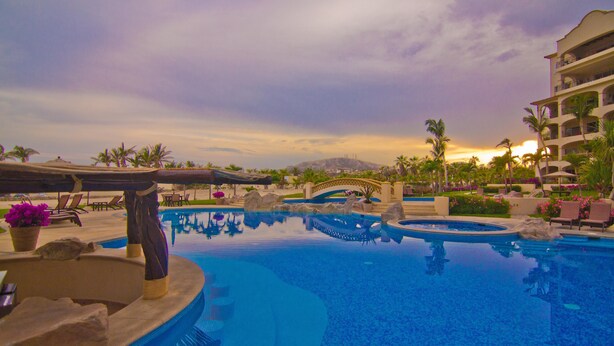 A resort pool with a bridge, palm trees, and a mountain in the background. - Las Mananitas LM BB2 2 Bedroom Condo By Seaside Los Cabos (San José del Cabo)