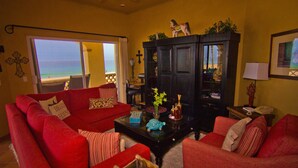 A living room with a red sofa, a black cabinet, and a view of the ocean through a door. - Las Mananitas LM BB2 2 Bedroom Condo By Seaside Los Cabos (San José del Cabo)