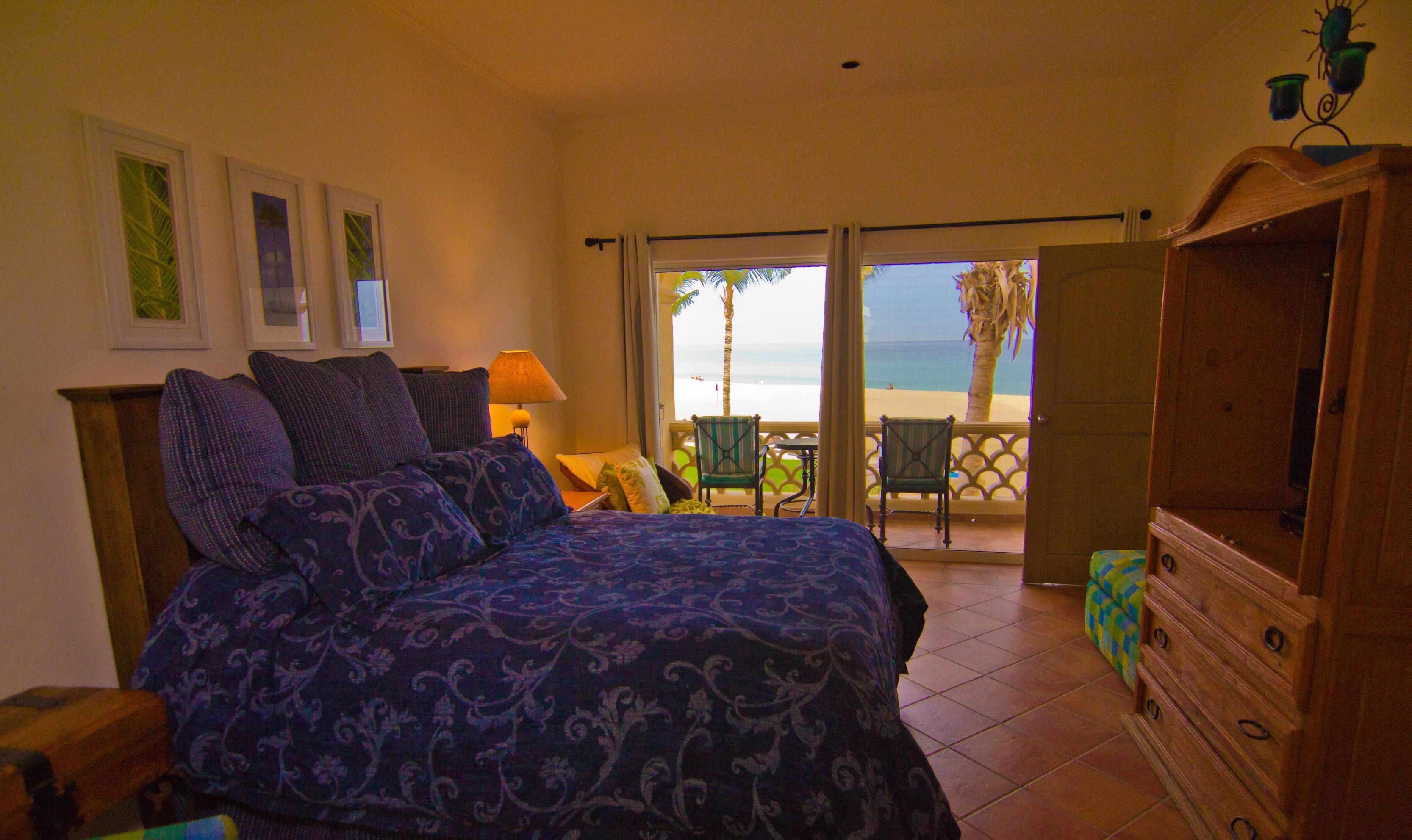 A bedroom with a bed, a dresser, a chair, and a view of the beach.