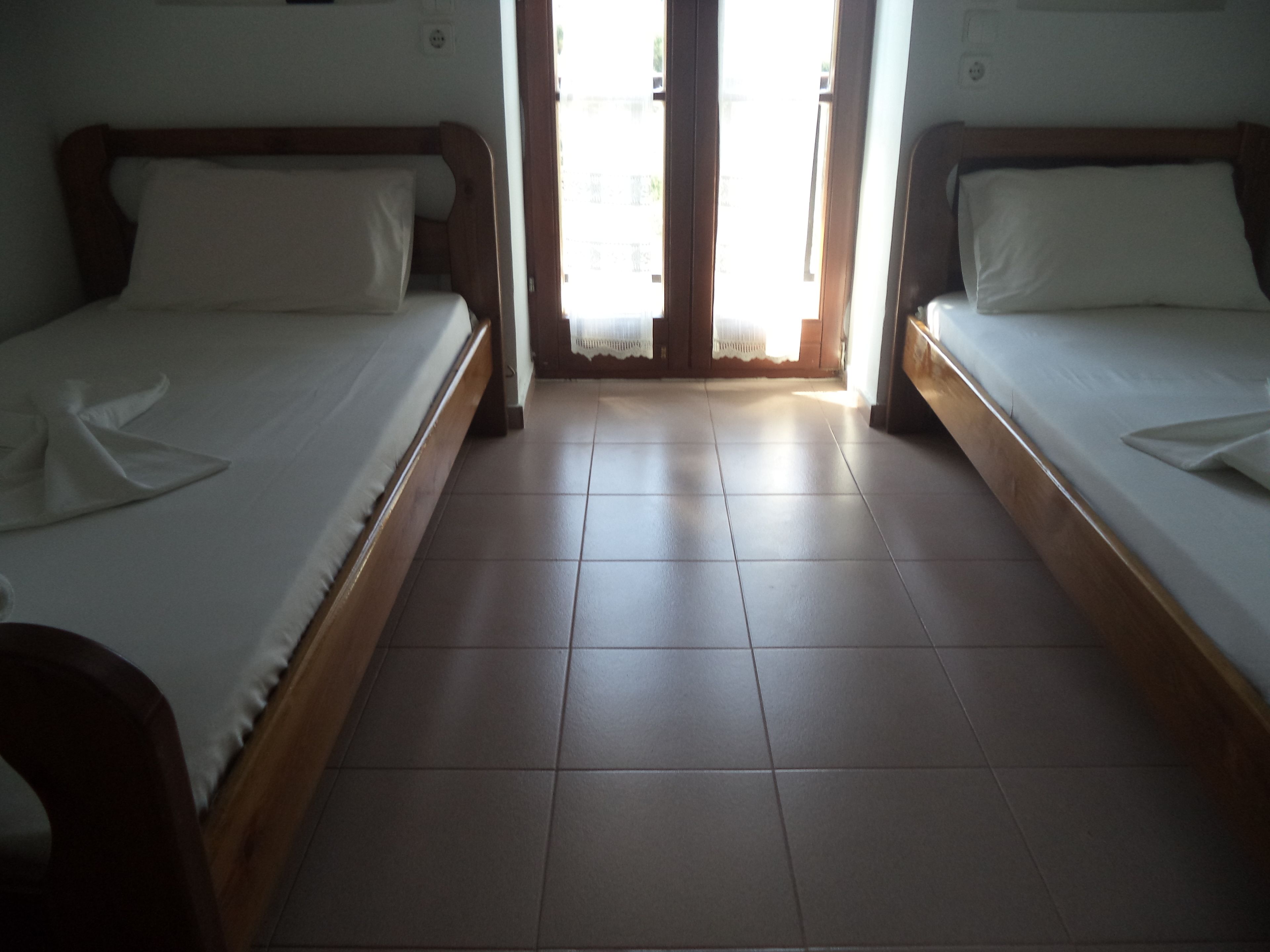 Una habitación de hotel con dos camas individuales, un cabecero de madera y piso de baldosas.