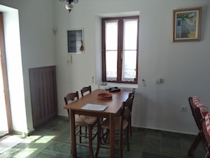 Un comedor con una mesa de madera, sillas, una ventana con cortinas de encaje, un cuadro enmarcado en la pared y una puerta con panel de madera.