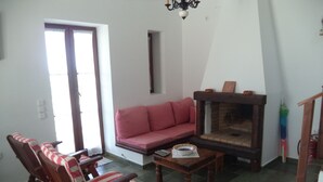 A living room with a sofa, a wooden chair, a fireplace, and a door. - Ilis Villas (Andravida-Kyllini)