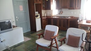 A compact kitchen with wooden cabinets, a built-in microwave, and a dining area with two chairs. - Ilis Villas (Andravida-Kyllini)