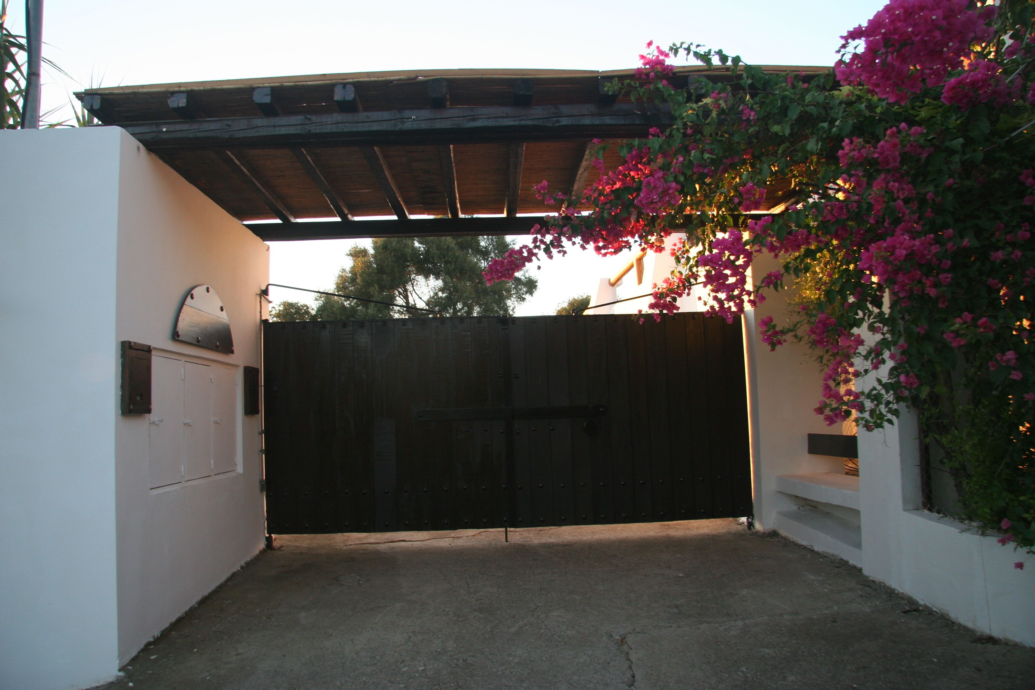 Una entrada portonada con piso de concreto, una pérgola de madera y un muro blanco con buzón.