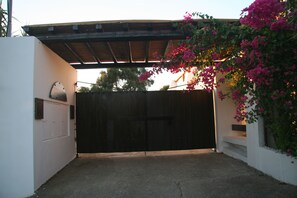 Una entrada portonada con piso de concreto, una pérgola de madera y un muro blanco con buzón.