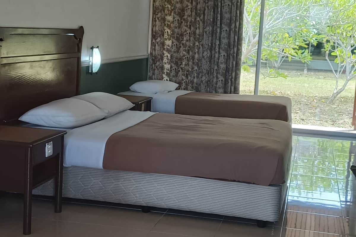 Une chambre d’hôtel avec un grand lit, un plus petit lit, une table de chevet et une fenêtre avec des rideaux.