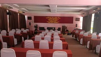 A conference room with rows of tables and chairs, a stage with a podium, and a banner with text.