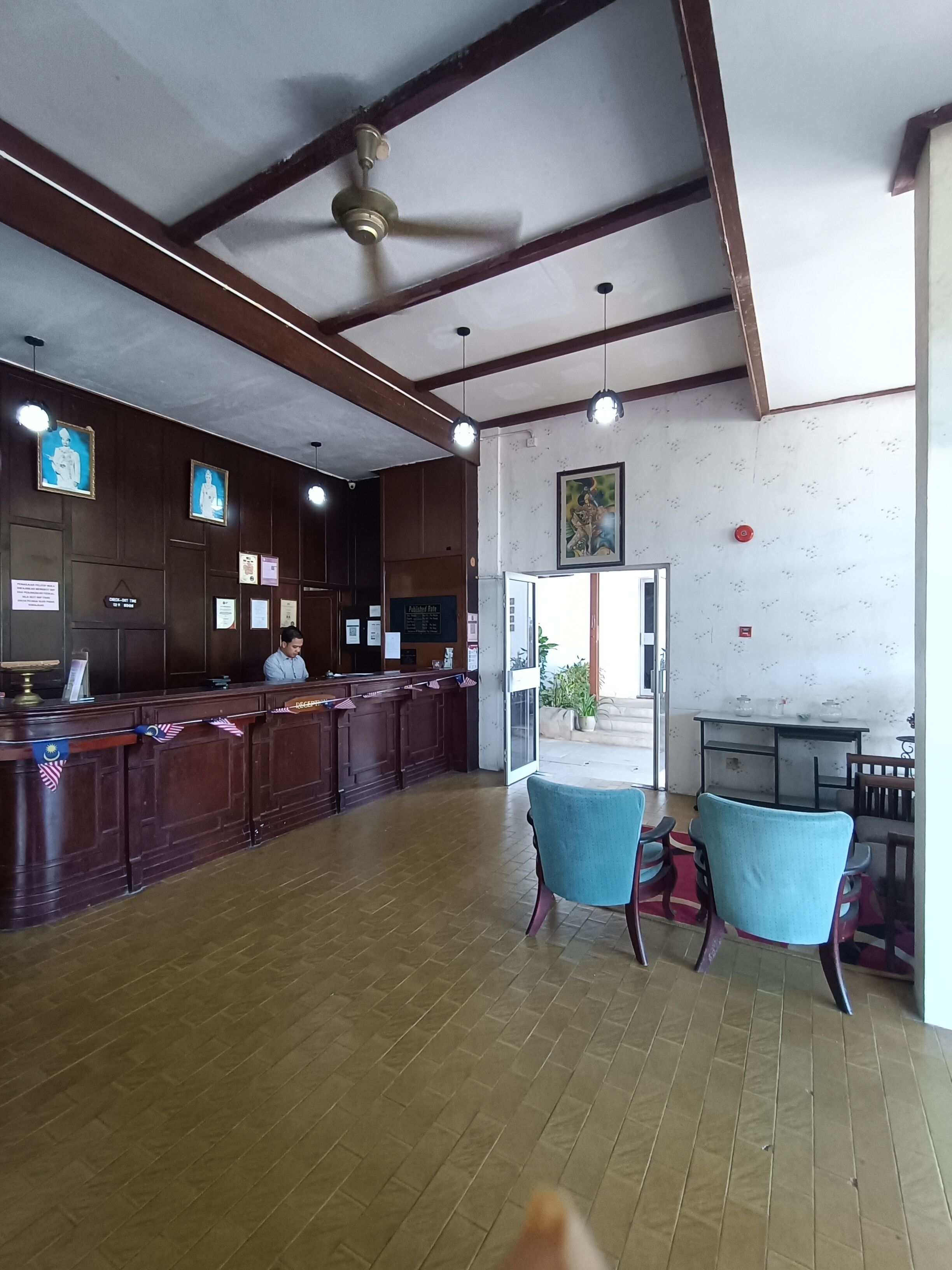 A reception area with a wooden counter, a ceiling fan, framed pictures on the wall, and a view of the outside.