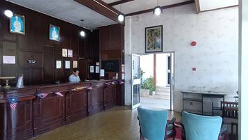 A reception area with a wooden counter, a ceiling fan, framed pictures on the wall, and a view of the outside.