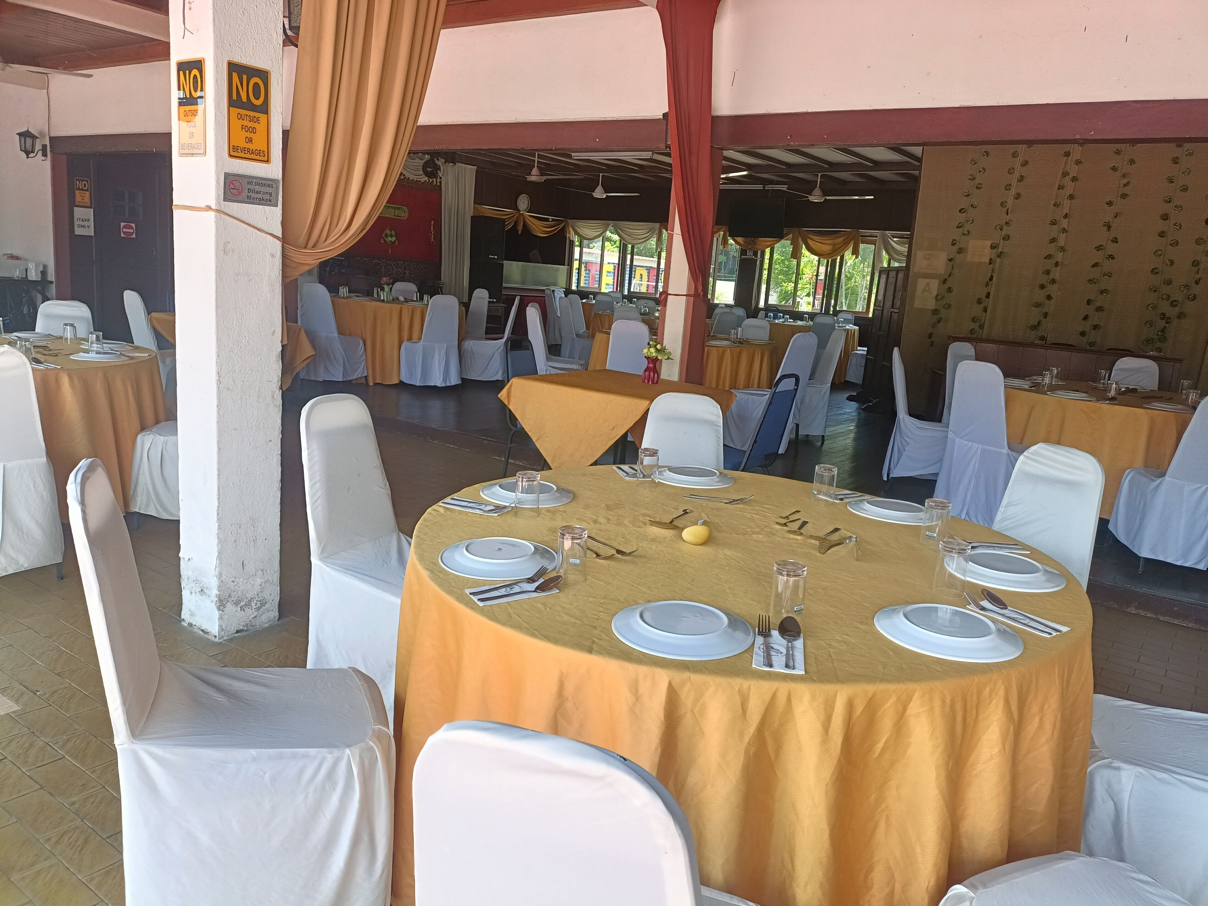 Une salle de banquet avec des tables rondes recouvertes de nappes jaunes, des chaises blanches et des tables dressées avec soin.