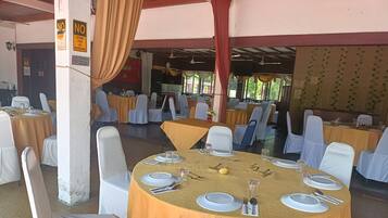 Salão de festas com mesas redondas cobertas por toalhas amarelas, cadeiras brancas e mesas de jantar bem postas.
