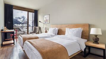 Habitación de hotel con dos camas, un escritorio, una silla, una lámpara y vistas a montañas nevadas.