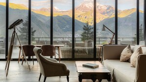 Una habitación con un amplio ventanal que ofrece vistas a la montaña, un telescopio, un sofá y una mesa.