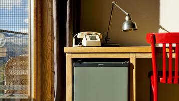 Een klein bureau met een antieke telefoon, een bureaulamp en een kleine koelkast.