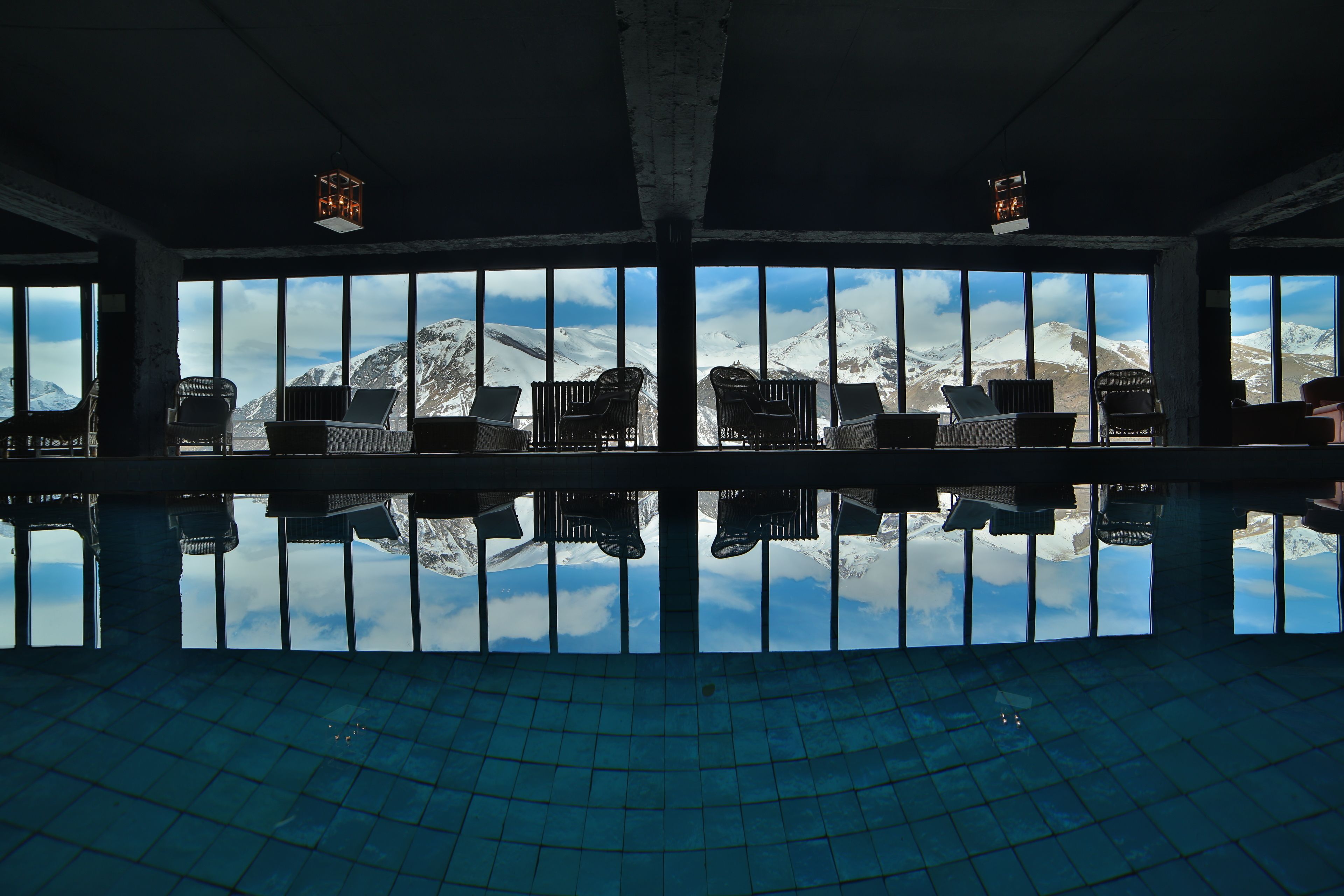 A pool area with chairs facing a large window overlooking snow-capped mountains.