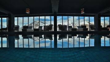 A pool area with chairs facing a large window overlooking snow-capped mountains.