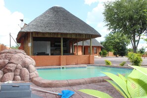 Ein Poolbereich mit einer strohgedeckten Struktur, einer Steinmauer und einem Pool mit Fliesenrand.