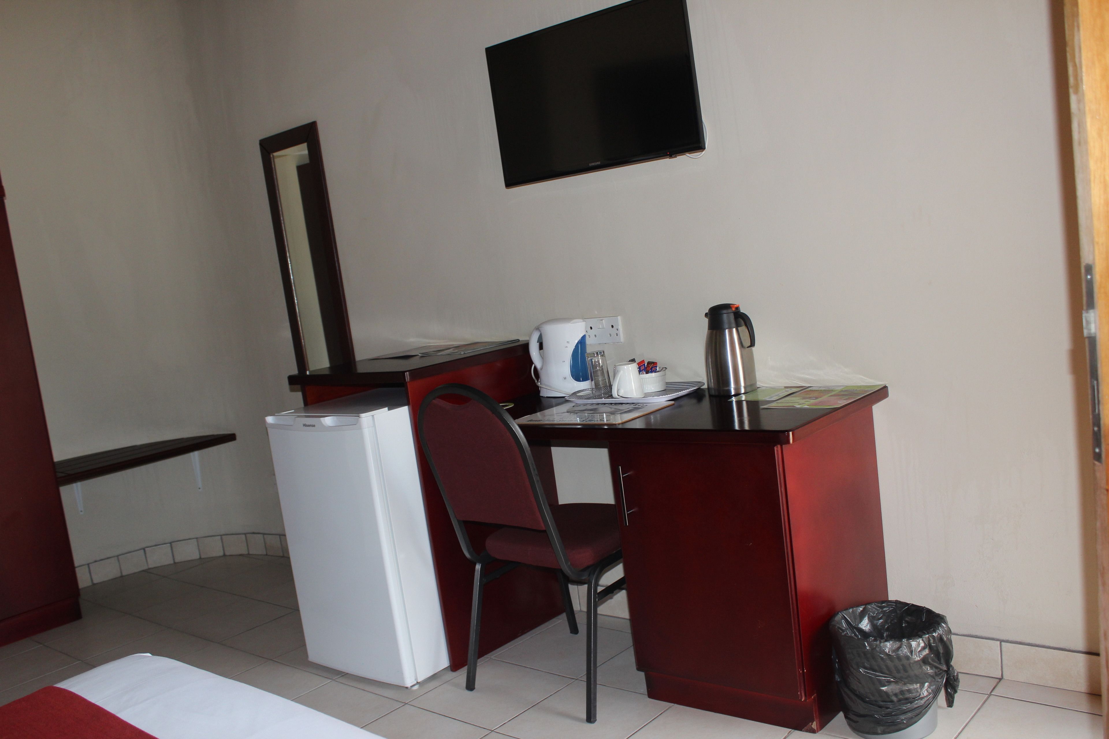 A compact room with a desk, chair, white refrigerator, and a mounted television.